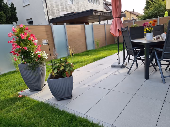 Terrasse aus großformatigen Betonplatten mit Esstisch, bepflanzten Kübeln und angrenzendem Rasen