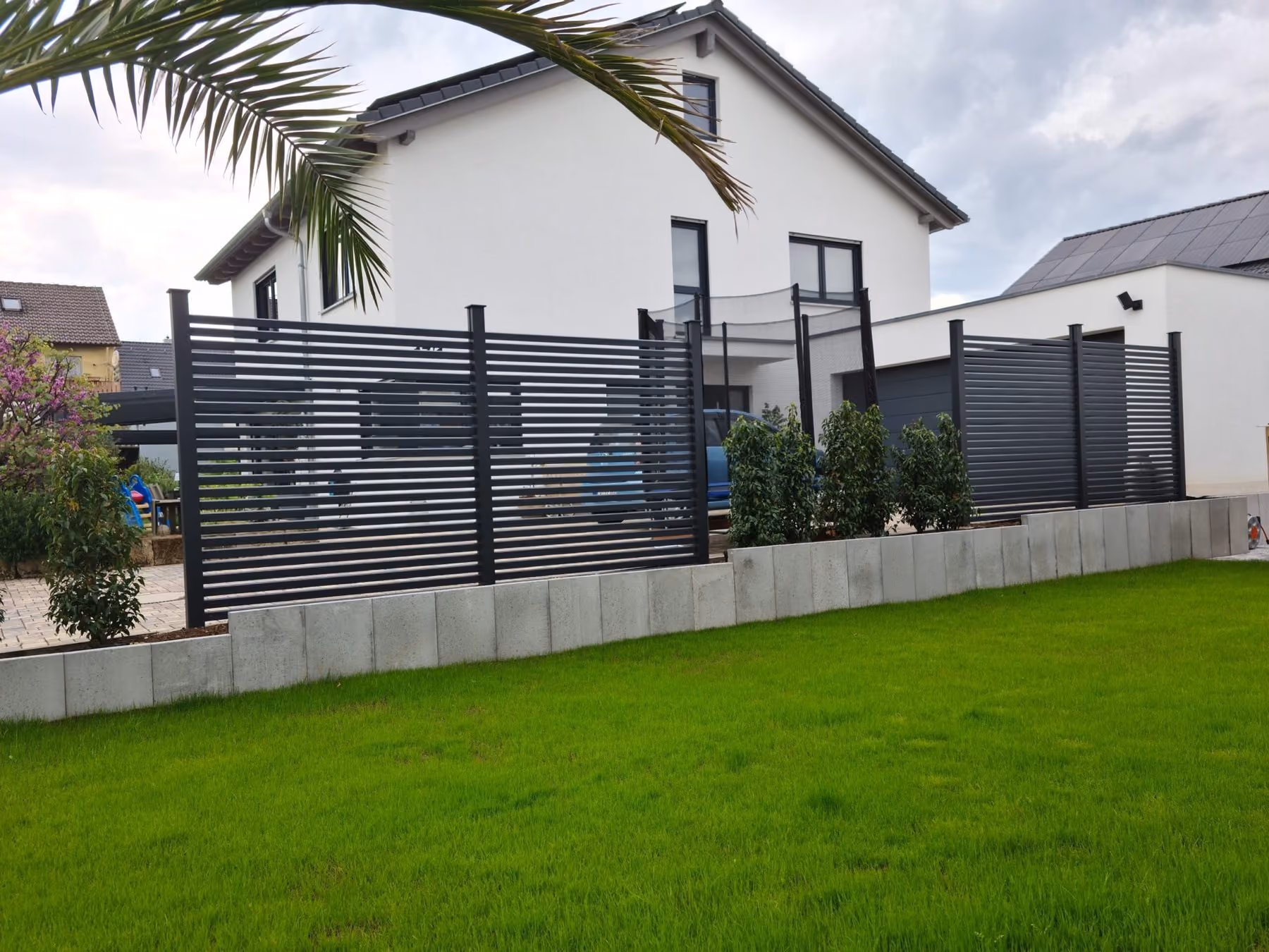 Frisch angelegter Rasen mit Betonrandstein und anthrazitfarbenem Lamellenzaun am Hausgrundstück