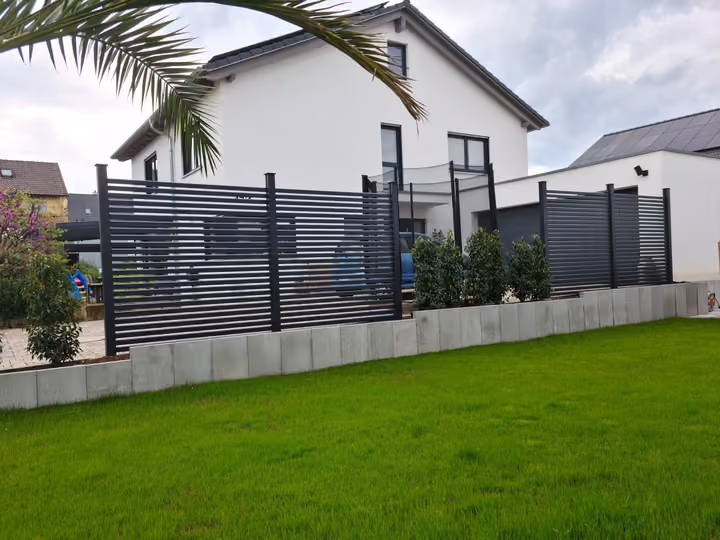 Frisch angelegter Rasen mit Betonrandstein und anthrazitfarbenem Lamellenzaun am Hausgrundstück