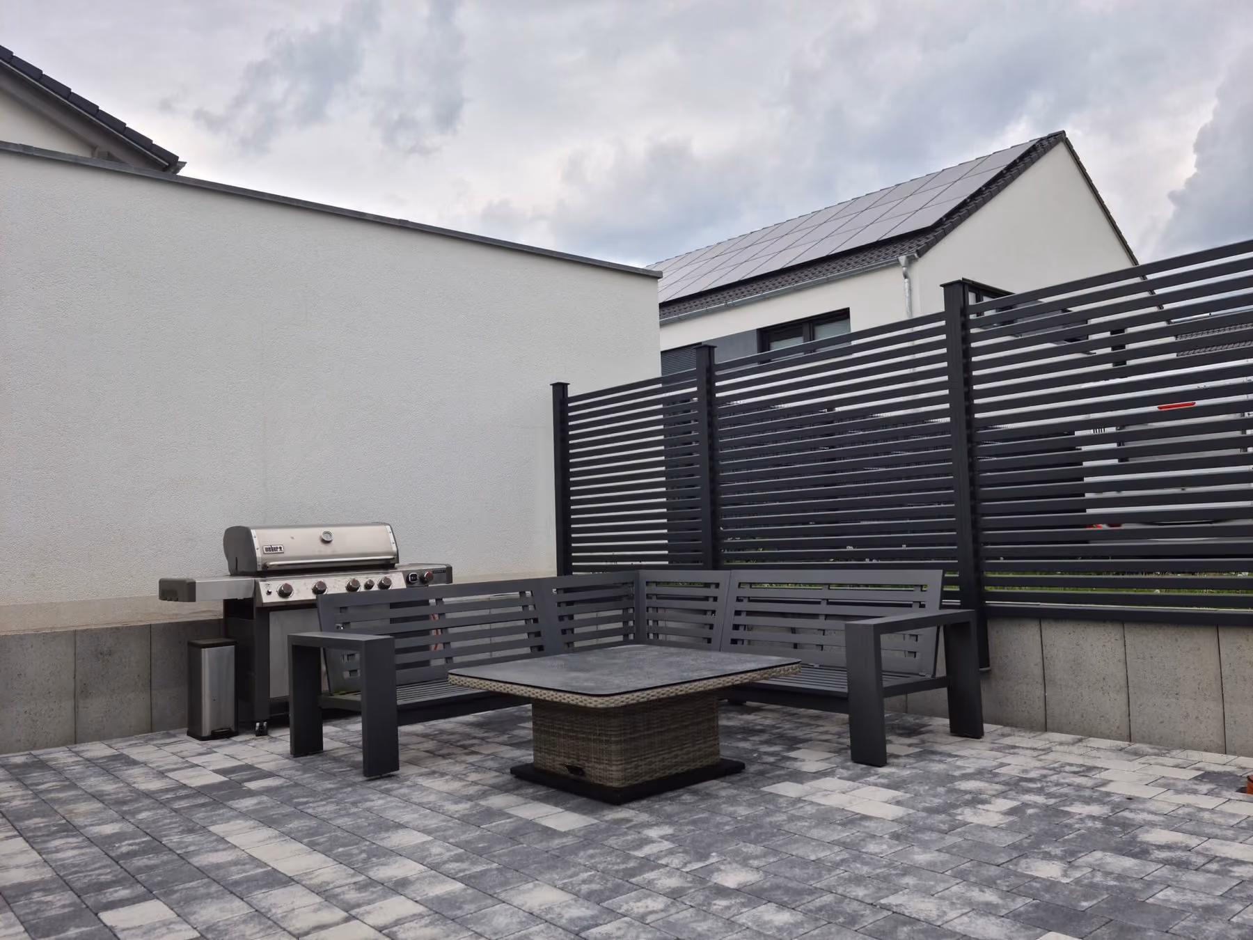 Grillplatz mit Sitzbank und Outdoor-Küche vor einem anthrazitfarbenen Sichtschutzelement