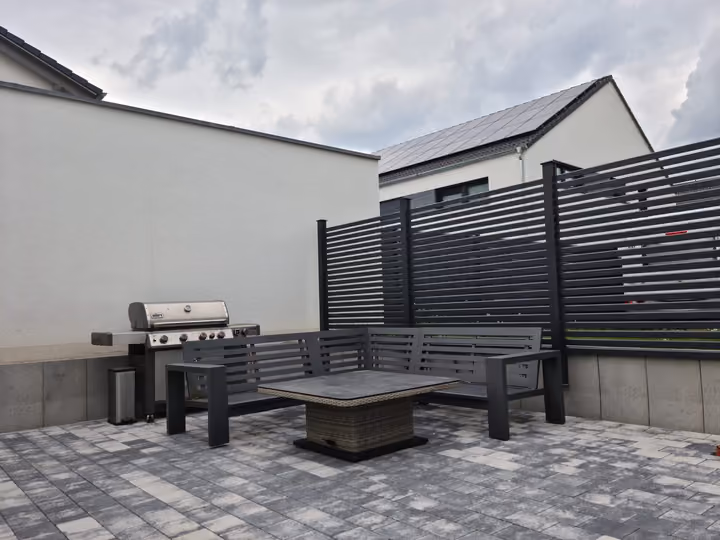 Grillplatz mit Sitzbank und Outdoor-Küche vor einem anthrazitfarbenen Sichtschutzelement