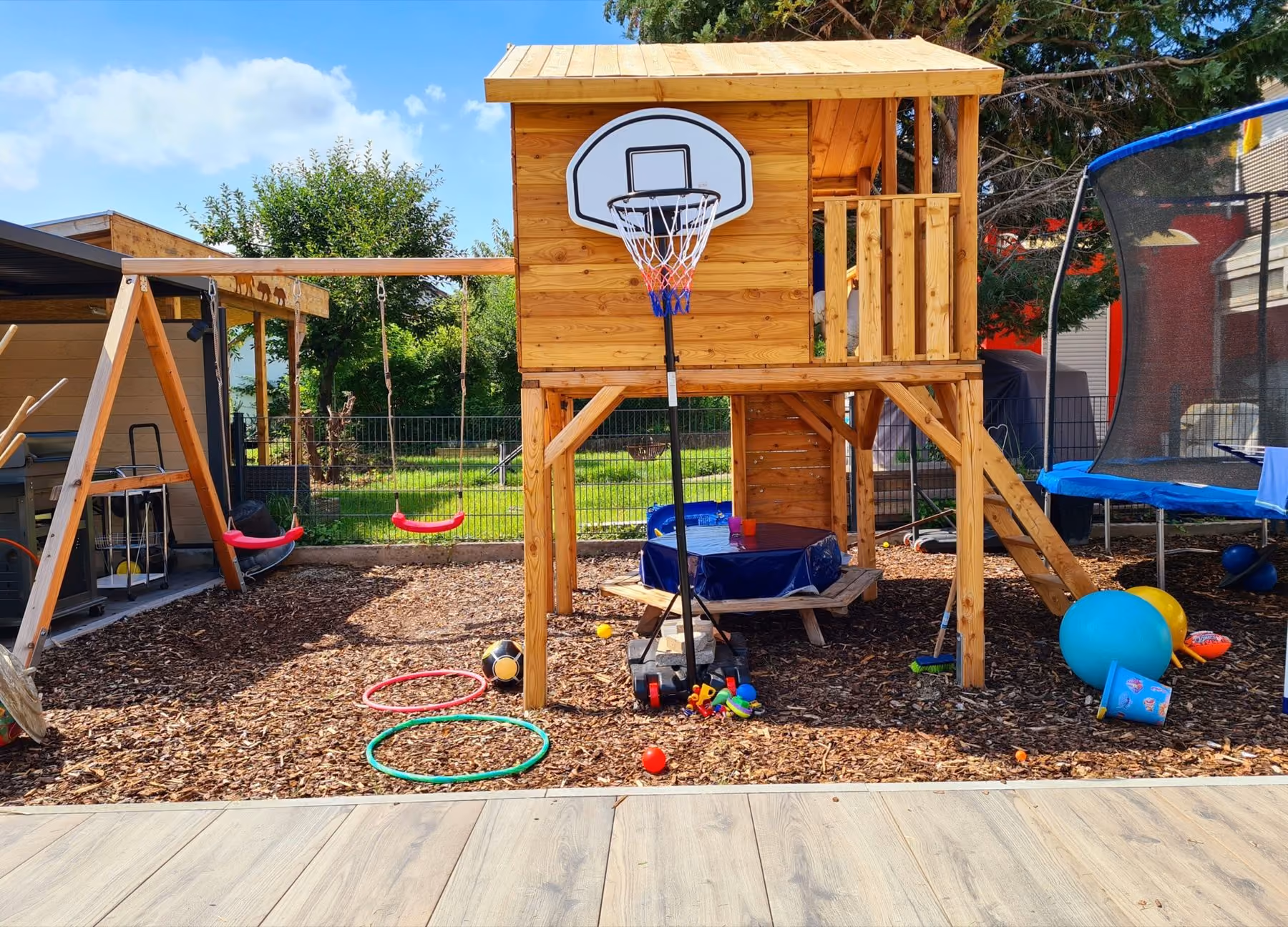 Spielturm mit Rutsche, Schaukel und Basketballkorb auf einer Fläche aus Rindenmulch