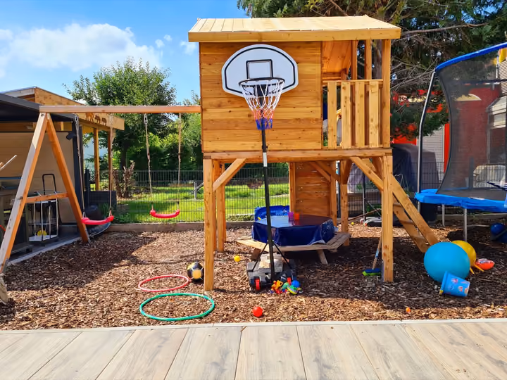 Spielturm mit Rutsche, Schaukel und Basketballkorb auf einer Fläche aus Rindenmulch