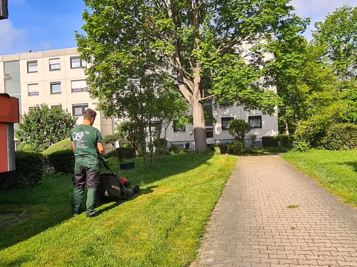 Mitarbeiter bei Rasenpflegearbeiten in der Grünanlage einer Wohnanlage