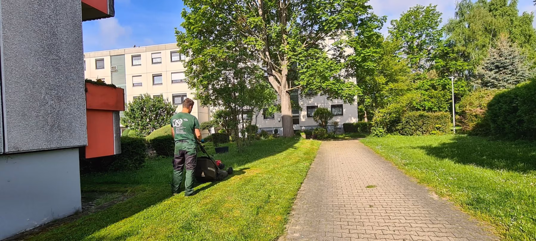 Mitarbeiter bei Rasenpflegearbeiten in der Grünanlage einer Wohnanlage