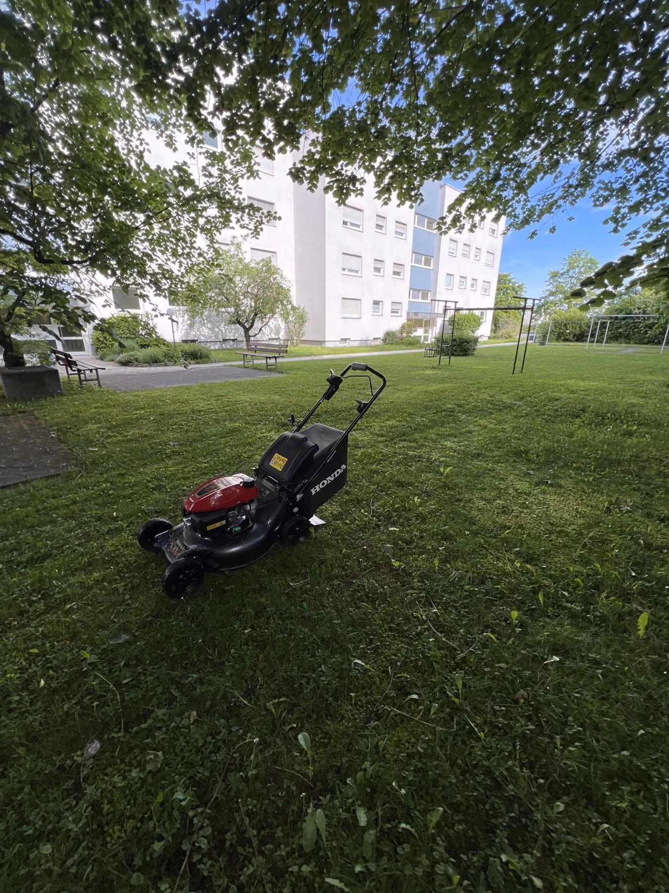 Rasenmäher auf einer frisch gemähten Grünfläche vor einem Mehrfamilienhaus