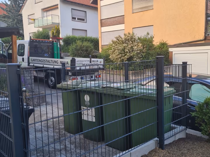 Eingefasster Müllplatz mit Metallzaun und Tor neben der Zufahrt einer Wohnanlage