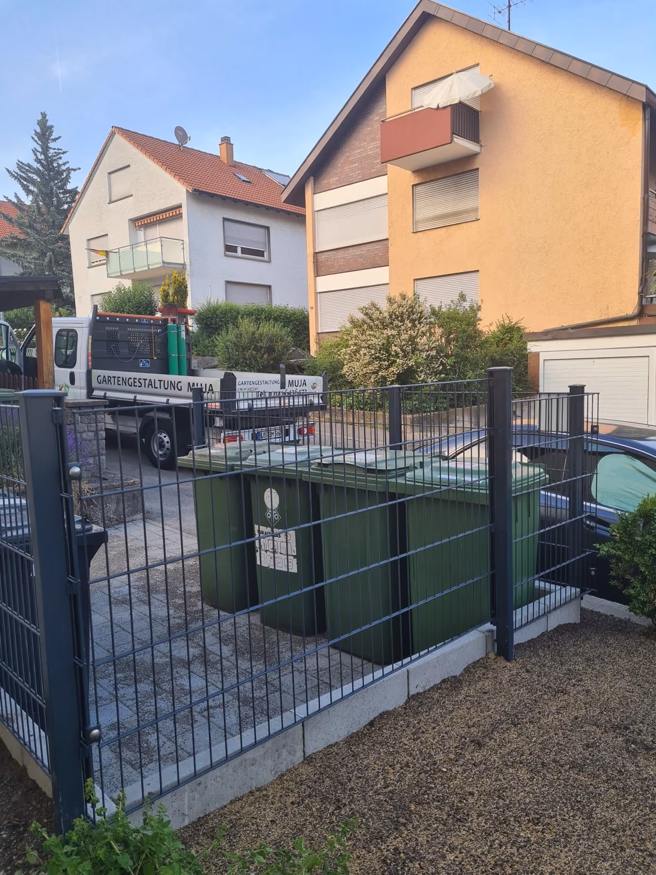 Eingefasster Müllplatz mit Metallzaun und Tor neben der Zufahrt einer Wohnanlage