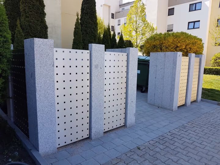 Müllplatzeinhausung aus gelochten Metallelementen zwischen Betonpfosten
