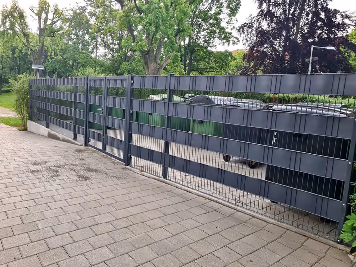 Langgestreckte Müllplatzeinhausung mit Sichtschutzstreifen entlang eines Zufahrtsweges