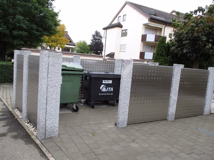 Müllplatz mit Edelstahl-Sichtschutzelementen zwischen Granitpfosten vor einem Wohnhaus