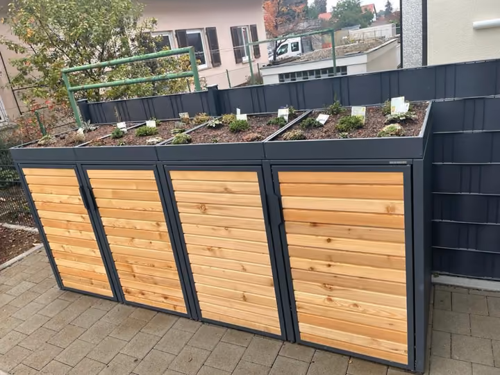 Müllplatzeinhausung mit Holzverkleidung und begrüntem Dach