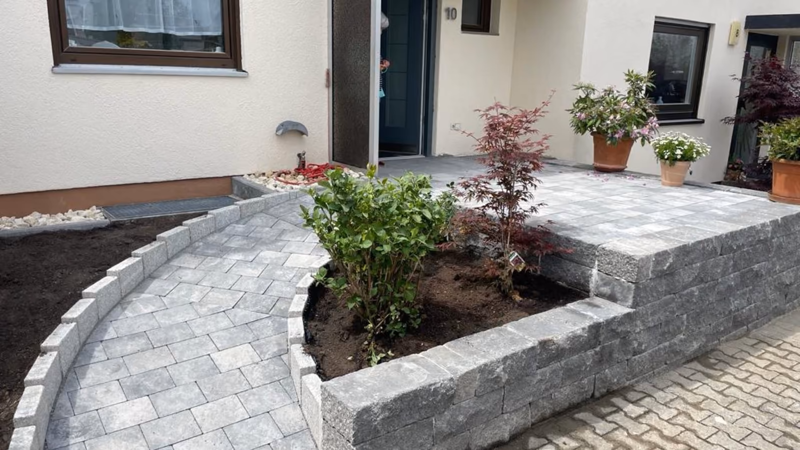 Halbrundes Hochbeet aus Granit-Kleinpflaster im Eingangsbereich eines Wohnhauses