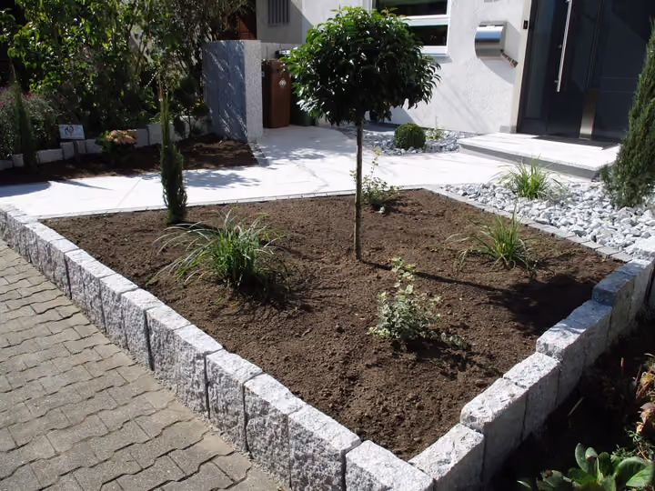 Beeteinfassung aus Granitsteinen mit frisch gesetztem Zierbaum und Kiesfläche
