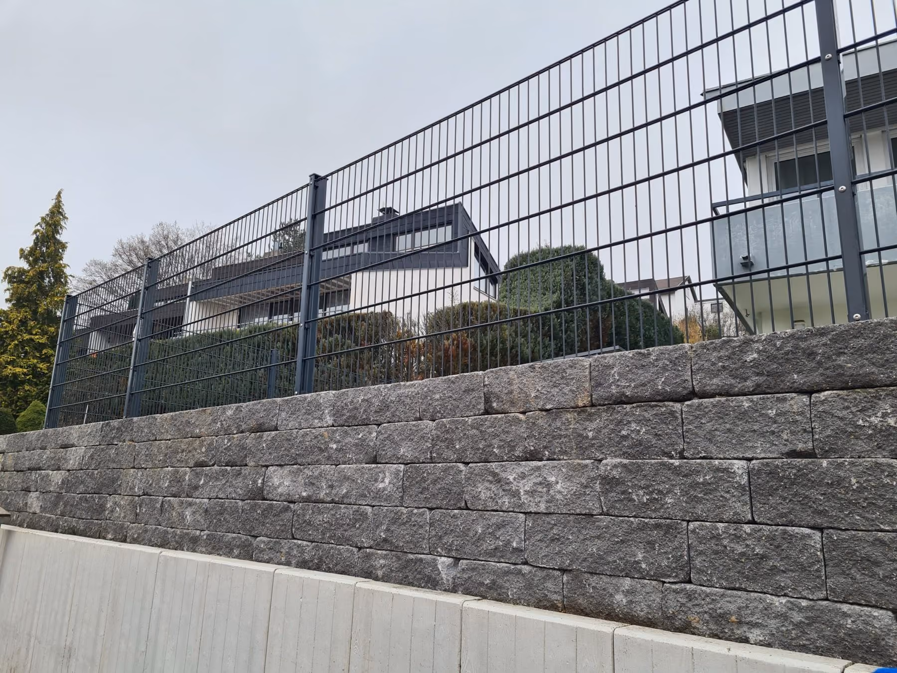 Trockenmauer aus geschichtetem Naturstein unterhalb eines Doppelstabmattenzauns