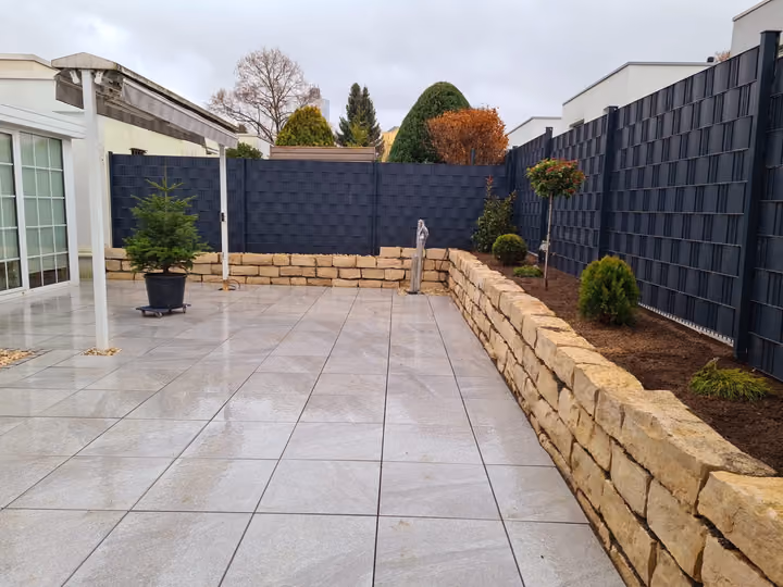 Terrasse mit heller Plattenfläche, eingefasst von einer niedrigen Natursteinmauer