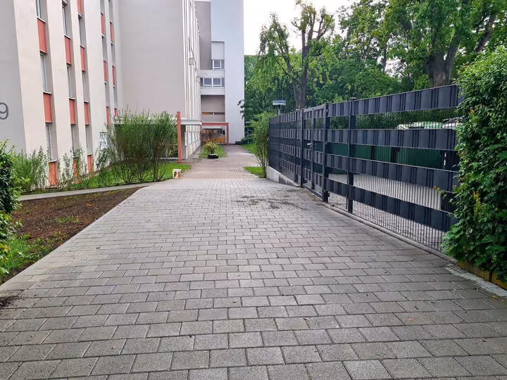 Gepflasterter Zufahrtsweg zwischen Mehrfamilienhaus und Sichtschutzzaun