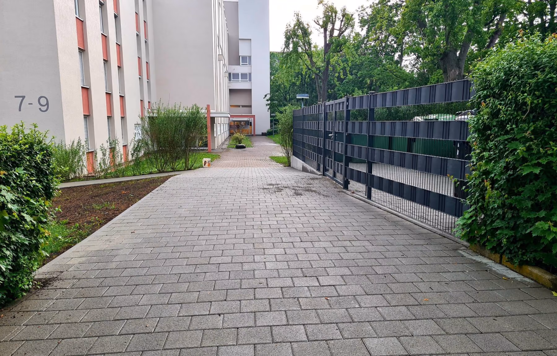 Gepflasterter Zufahrtsweg zwischen Mehrfamilienhaus und Sichtschutzzaun