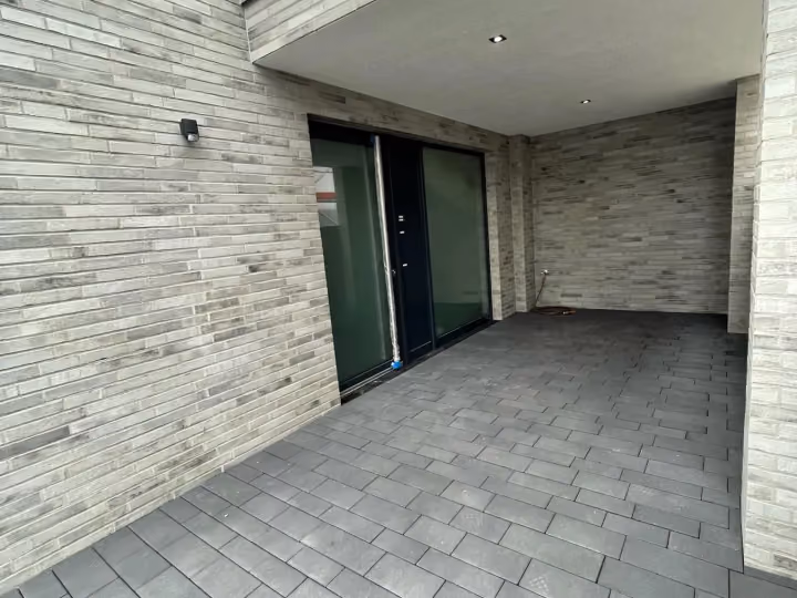 Überdachter Eingangsbereich mit hellem Feinsteinzeug-Belag an einem modernen Wohnhaus