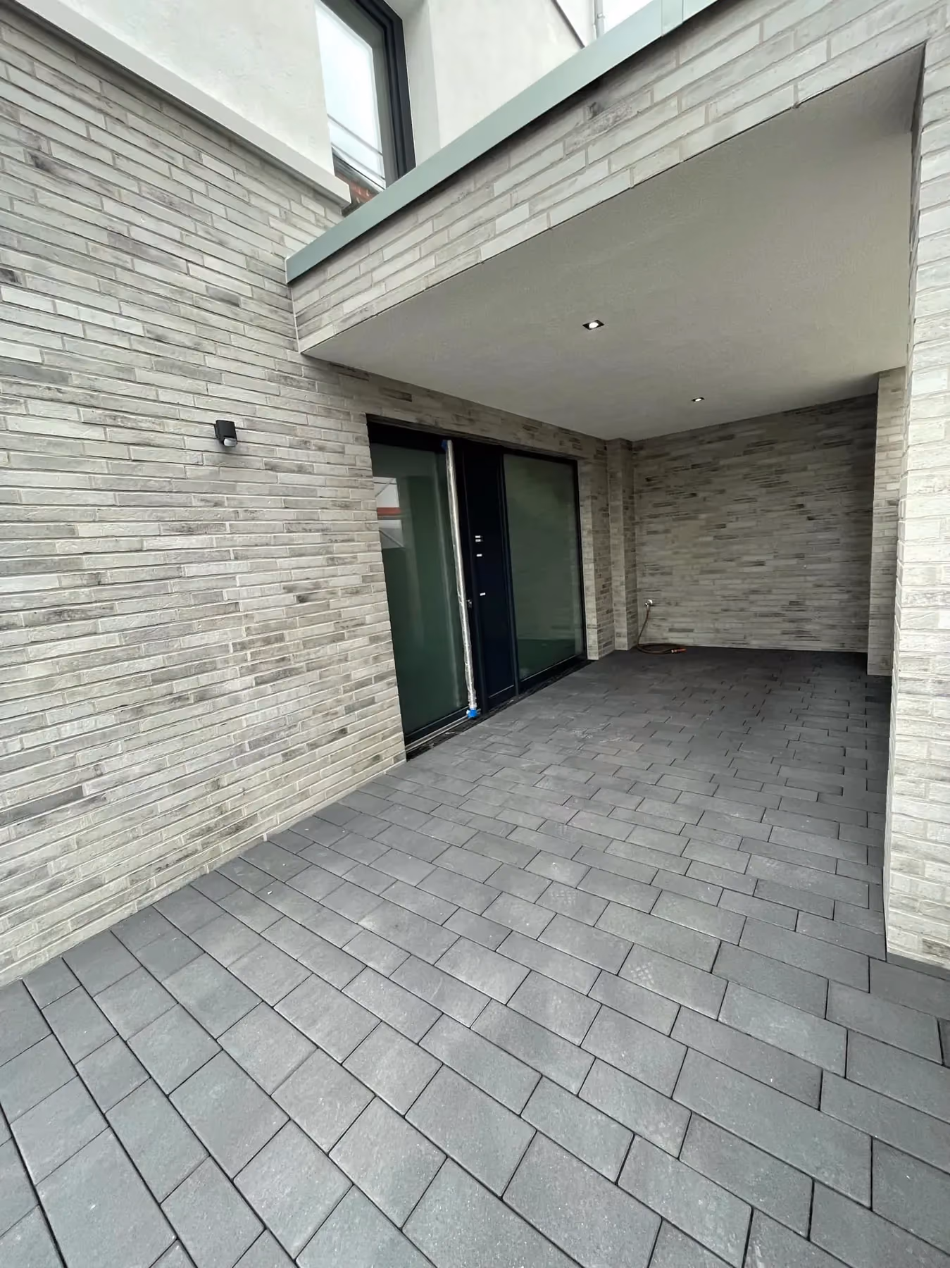 Überdachter Eingangsbereich mit hellem Feinsteinzeug-Belag an einem modernen Wohnhaus