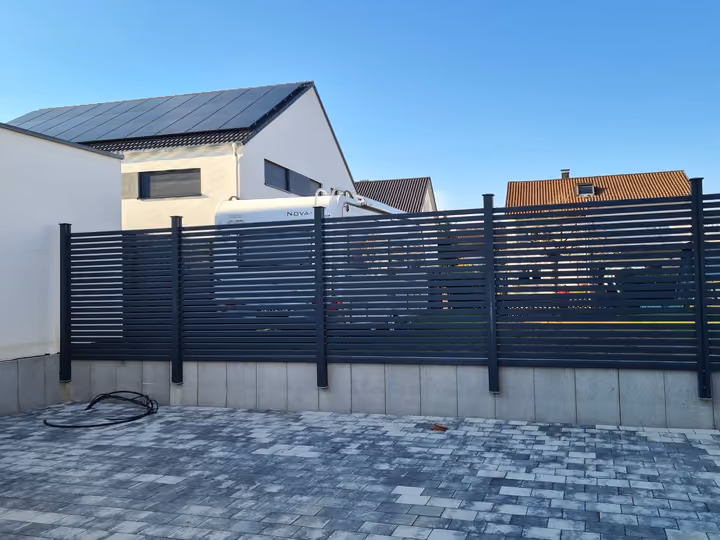 Gepflasterter Stellplatz mit anthrazitfarbenem Lamellenzaun vor einem Einfamilienhaus