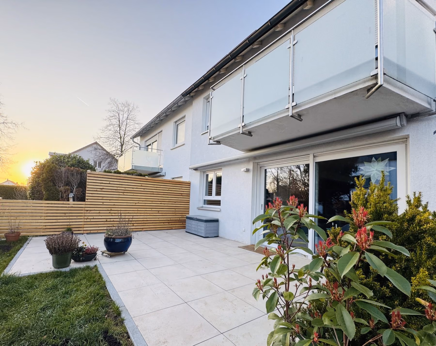 Terrasse aus hellen Platten mit Sichtschutz und bepflanzten Kübeln im Abendlicht