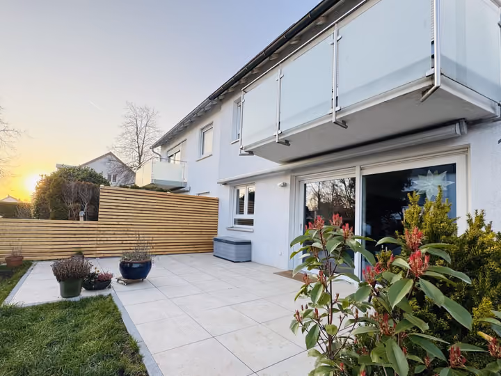 Terrasse aus hellen Platten mit Sichtschutz und bepflanzten Kübeln im Abendlicht
