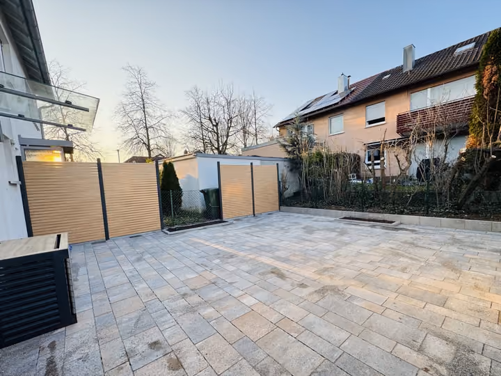 Breite gepflasterte Einfahrt mit hellem Holzsichtschutz in der Abenddämmerung