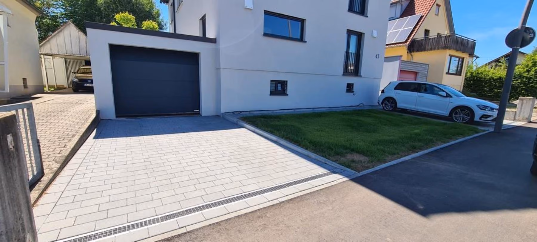 Gepflasterte Einfahrt vor einer Garage, seitlich begrenzt von einem Rasenstreifen