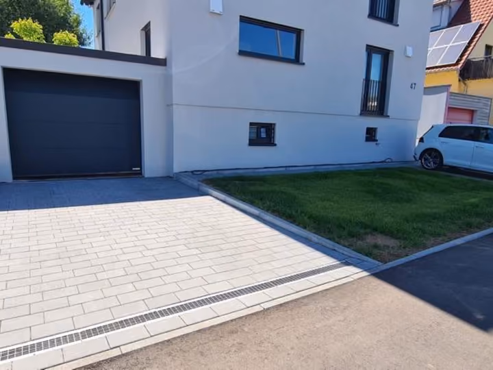Gepflasterte Einfahrt vor einer Garage, seitlich begrenzt von einem Rasenstreifen