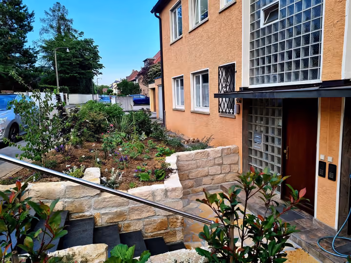 Sandsteintreppe mit Edelstahlgeländer als Hauszugang zwischen bepflanzten Beeten