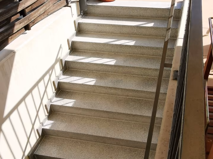 Schmale Außentreppe mit Handlauf entlang einer Hauswand, oben mit Holzsichtschutz