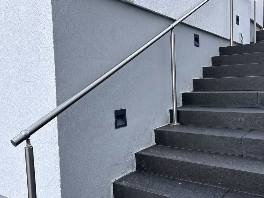 Sanierte Außentreppe mit Steinteppich-Belag und Edelstahlhandlauf an einer weißen Hauswand