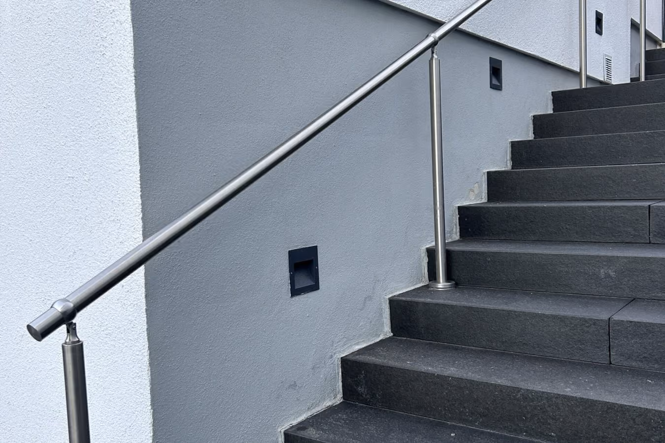 Sanierte Außentreppe mit Steinteppich-Belag und Edelstahlhandlauf an einer weißen Hauswand