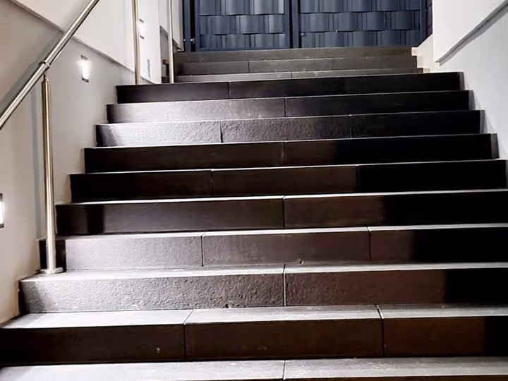 Beleuchteter Hauseingang mit dunklen Stufen und seitlichem Geländer bei Nacht
