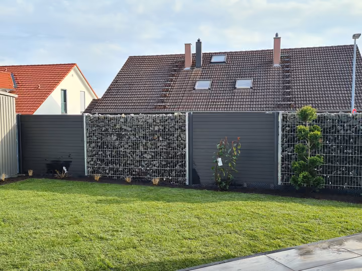 Kombination aus Gabionenwand und anthrazitfarbenen Sichtschutzelementen entlang einer Rasenfläche