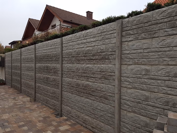 Hohe Betonsichtschutzwand in Holzstruktur entlang einer Grundstücksgrenze am Hang