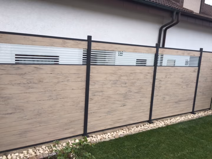 Sichtschutzzaun in heller Holzoptik mit Lamellenaufsatz an einer Hauswand